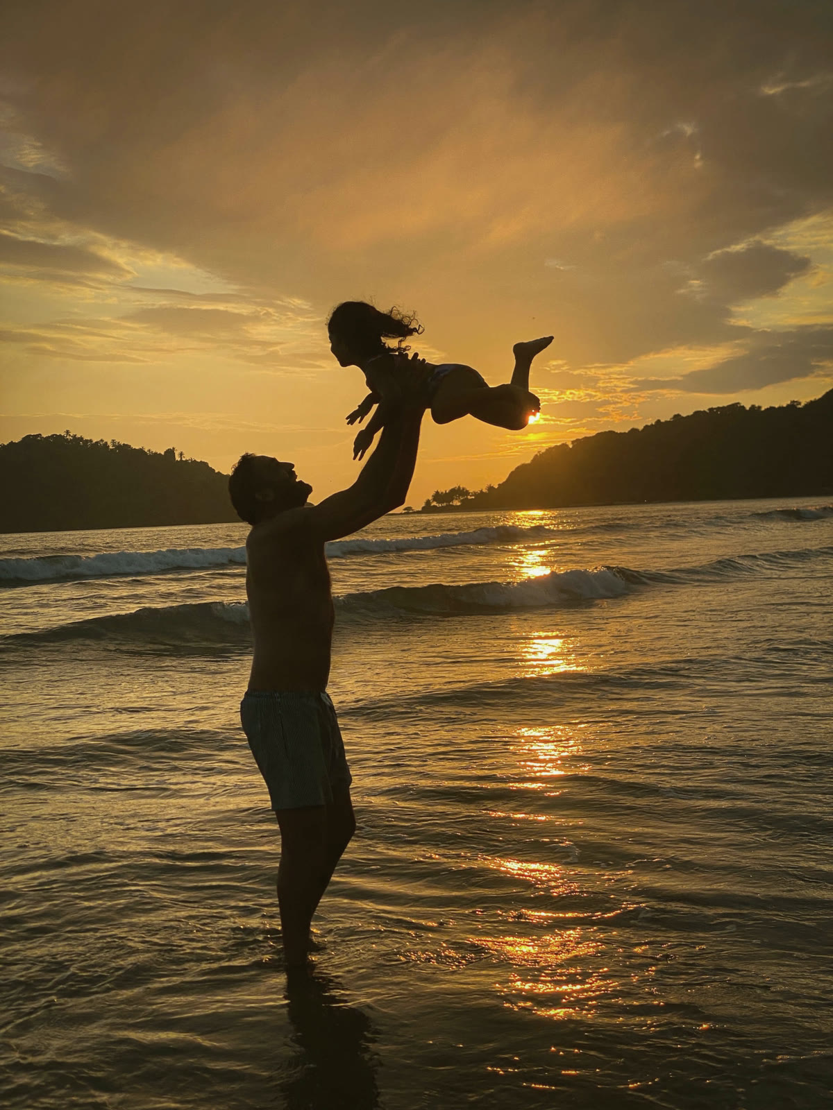 A parent lifting a child into the sunset